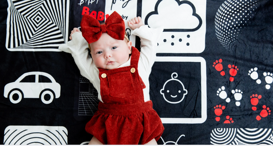 Baby lying on a high-contrast black, white, and red Baby Geometrics floor blanket during tummy time to support early visual and motor development.