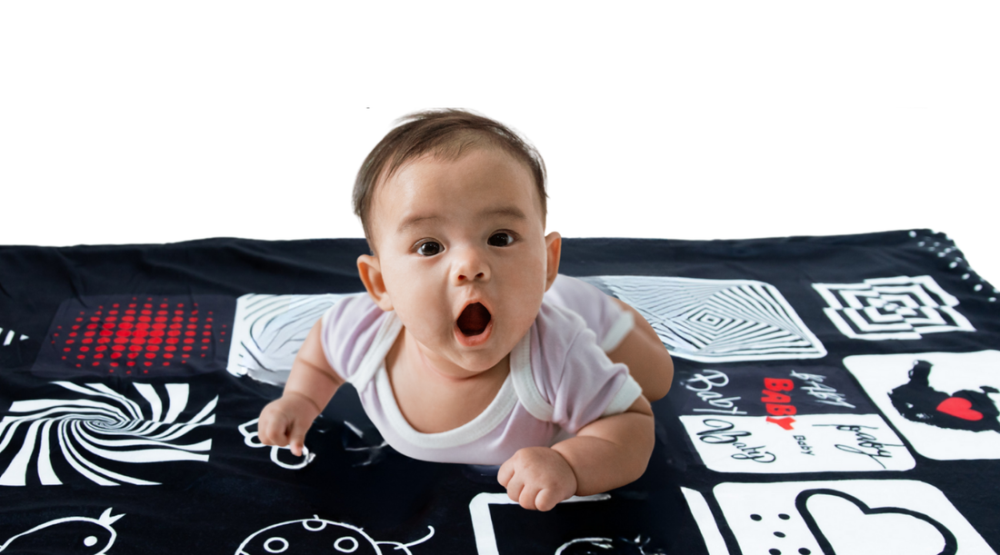 Baby lying on tummy on a high-contrast blanket, lifting head and engaging in tummy time to promote brain and visual development.