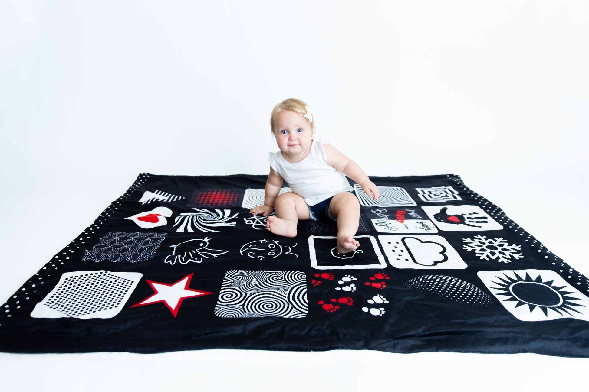 Baby sitting happily on the Baby Geometrics floor blanket, featuring high-contrast patterns designed to stimulate visual development and provide a soft, spacious surface for playtime.