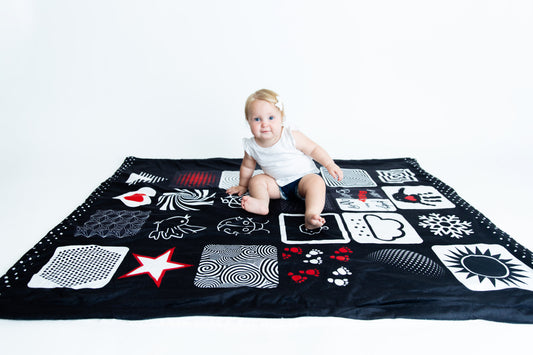 Baby sitting happily on the Baby Geometrics floor blanket, featuring high-contrast patterns designed to stimulate visual development and provide a soft, spacious surface for playtime.