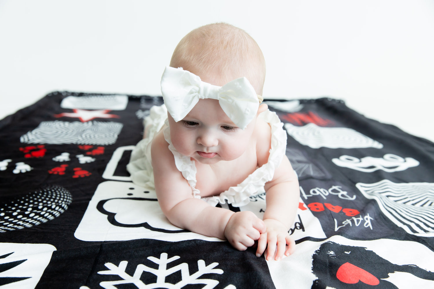 Baby gazing down at the bold black-and-white patterns on the Baby Geometrics floor blanket, actively engaging their developing vision and focus.