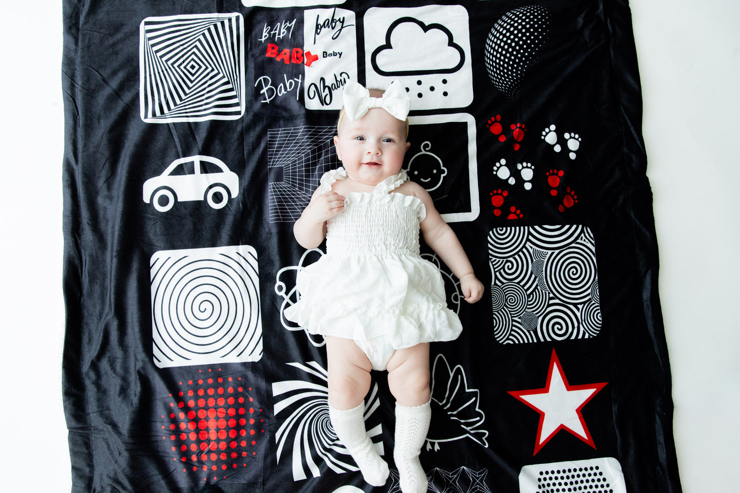 Baby laying down on the bold black-red and-white patterned baby blanket. A cozy place to relax and engage. 