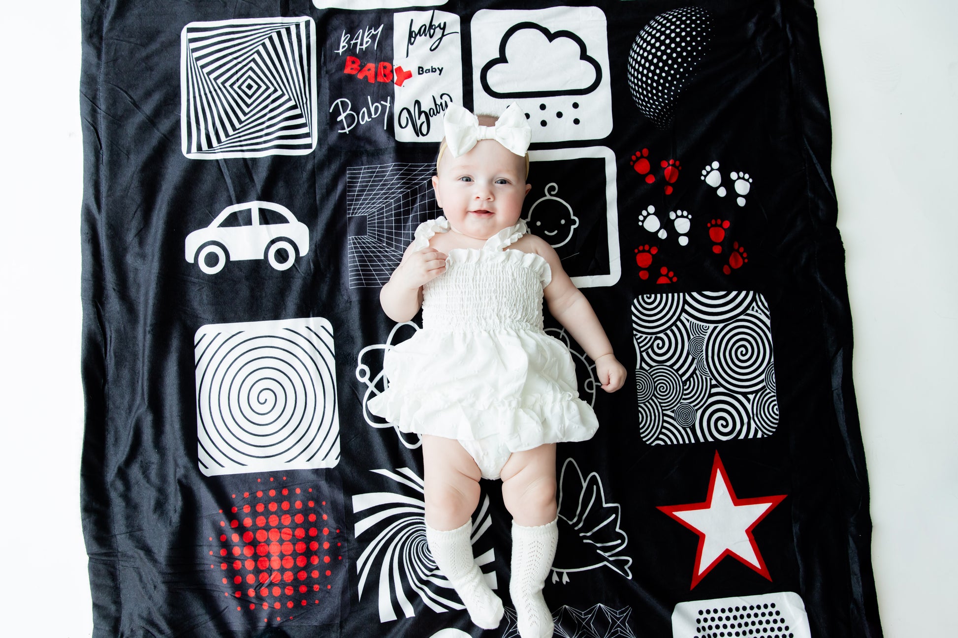 Baby laying down on the bold black-red and-white patterned baby blanket. A cozy place to relax and engage. 